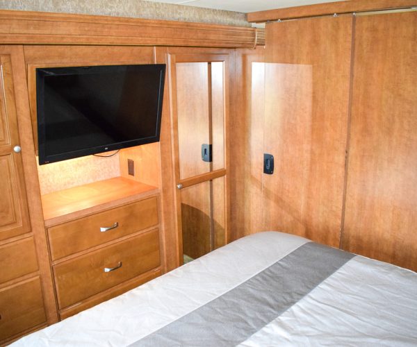 A bedroom with a bed, tv and cabinet.