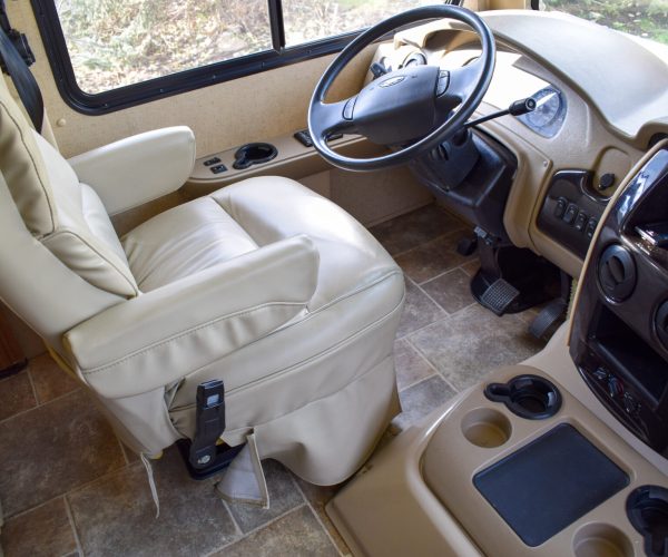 A white rv with a tan leather seat and a steering wheel.