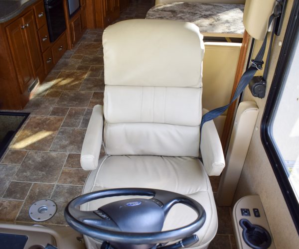 A white leather chair and steering wheel in the middle of an rv.