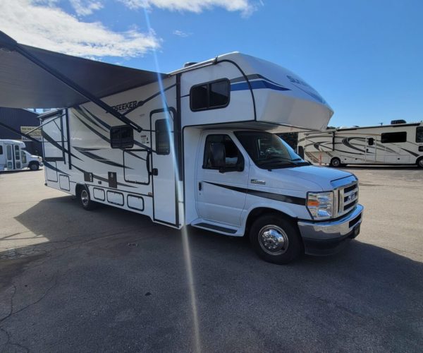 A white rv parked in the lot under an awning.