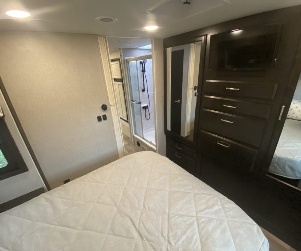 A bed room with a white bedspread and a black dresser