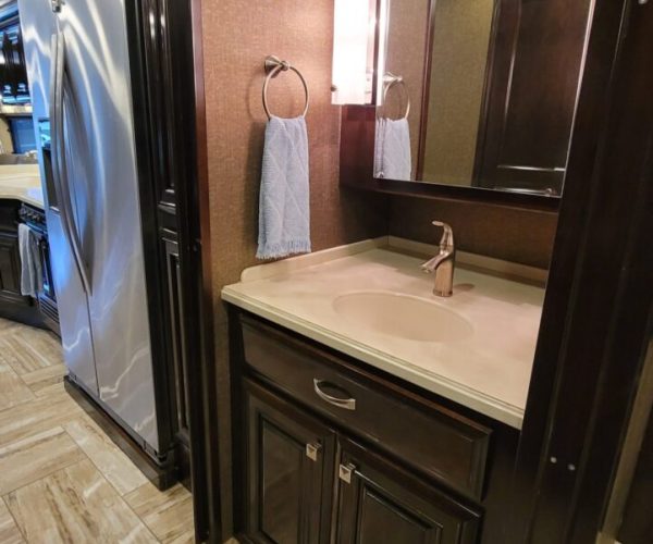 A bathroom with a sink, mirror and a refrigerator.