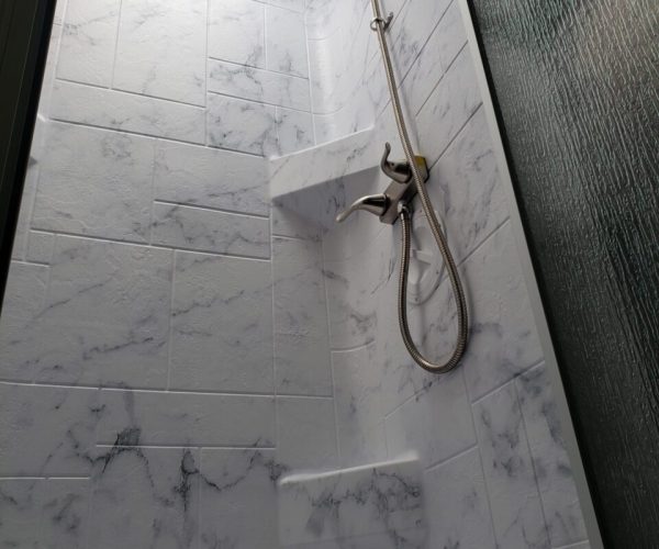 A bathroom with marble tile and a shower head.